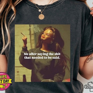 K&ouml;nnte beinhalten: Dunkelgraues T-Shirt mit einem quadratischen Grafik einer Puppe, die eine Zigarette raucht, und dem Text "Me after saying the shit that needed to be said." Das T-Shirt hat einen Rundhalsausschnitt und kurze &Auml;rmel.