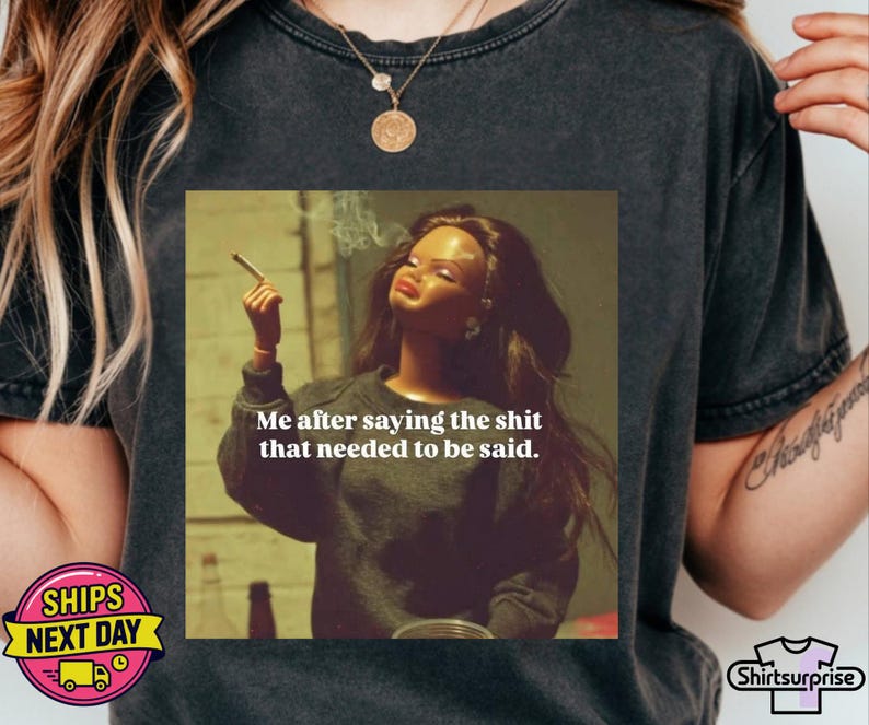 K&ouml;nnte beinhalten: Dunkelgraues T-Shirt mit einem quadratischen Grafik einer Puppe, die eine Zigarette raucht, und dem Text "Me after saying the shit that needed to be said." Das T-Shirt hat einen Rundhalsausschnitt und kurze &Auml;rmel.