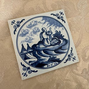 Könnte beinhalten: Quadratische Keramikfliese mit einer blau-weißen Illustration einer Person in einem Boot, umgeben von Wolken und Wasser. Die Fliese hat einen dekorativen Rand mit floralen Akzenten und dem Text "EX 10:30".