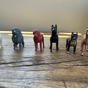 May include: Six plastic toy dogs in various poses and colors, including white, gray, red, black, and brown. The dogs are standing on a wooden surface.