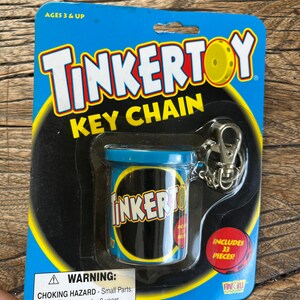 May include: A blue and yellow Tinkertoy keychain with a small plastic container that includes 33 pieces. The packaging says "Ages 3 & Up" and "WARNING: CHOKING HAZARD - Small Parts. Not for children under 3 years."