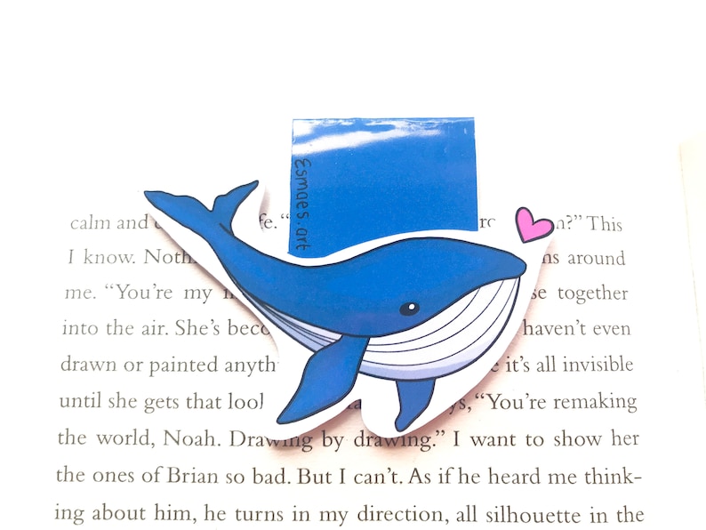 Op de afbeelding: Een blauwe walvis-bladwijzer met een witte buik en een roze hart. De bladwijzer is gemaakt van papier en heeft een glanzende afwerking. De tekst "Esmaes.art" is op de bladwijzer gedrukt.
