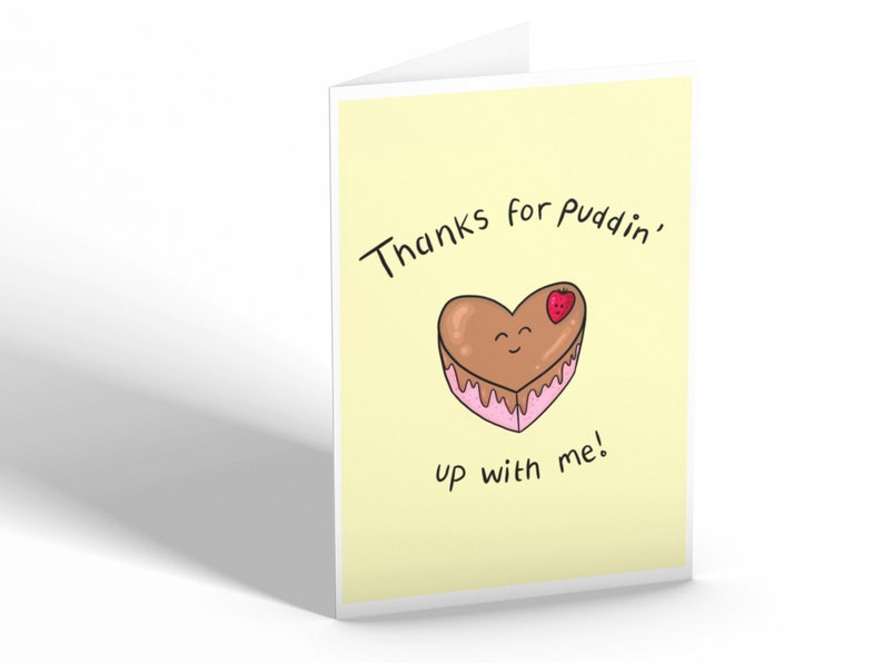 May include: A yellow card with the text "Thanks for puddin' up with me!" and a cartoon heart-shaped chocolate cake with pink frosting and a strawberry on top.