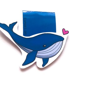 Op de afbeelding: Een blauwe walvis-bladwijzer met een roze hart. De bladwijzer heeft de tekst "Esme's Art" erop.