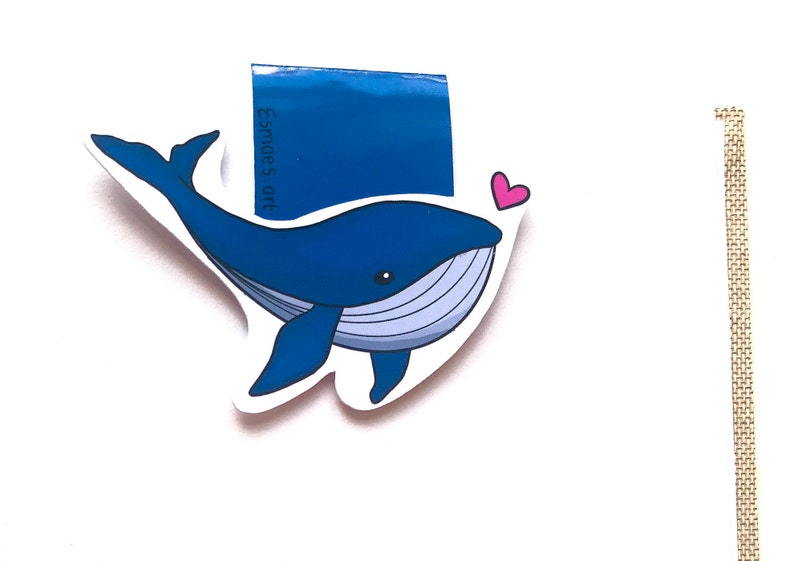 Op de afbeelding: Een blauwe walvis-bladwijzer met een roze hart. De bladwijzer heeft de tekst "Esme's Art" erop.