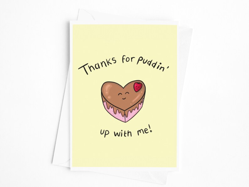 May include: A yellow card with the text "Thanks for puddin' up with me!" and a cartoon heart-shaped chocolate cake with a strawberry on top.