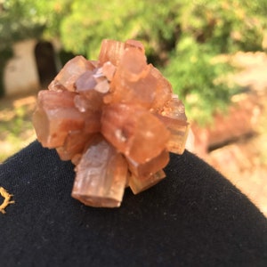 Pu&ograve; includere: Un gruppo di piccoli cristalli di colore arancio-marrone con una superficie ruvida e testurizzata. I cristalli sono disposti in una forma circolare, che ricorda un fiore.