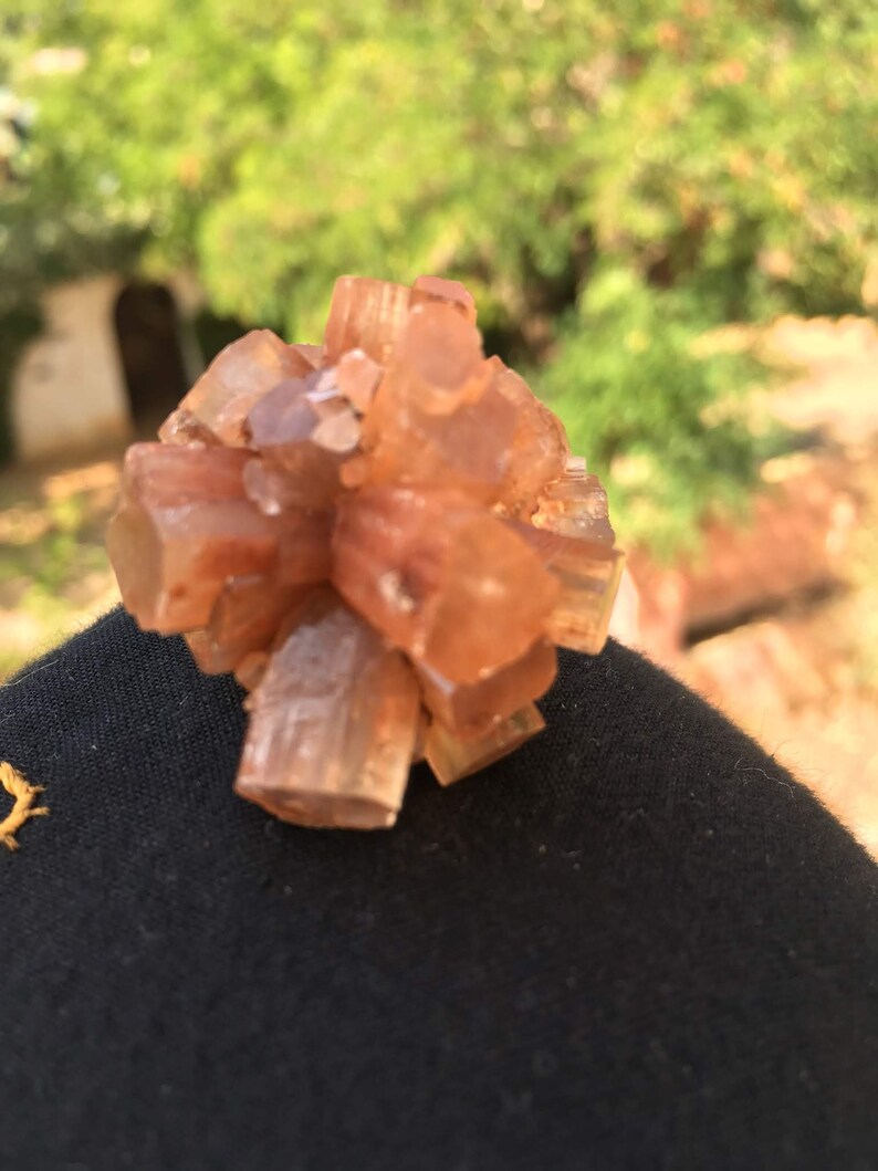 Pu&ograve; includere: Un gruppo di piccoli cristalli di colore arancio-marrone con una superficie ruvida e testurizzata. I cristalli sono disposti in una forma circolare, che ricorda un fiore.