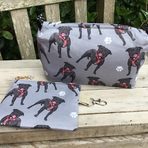 May include: Two grey zippered pouches with a black and white paw print and black dog pattern. The larger pouch is standing upright and the smaller pouch is lying flat. Both pouches have a zipper closure.