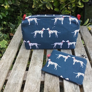 May include: Two zippered pouches with a teal blue background and a white dalmatian dog print. The larger pouch has red zipper pulls and the smaller pouch has a red zipper pull and a silver zipper pull.