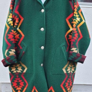 May include: A green wool coat with a geometric pattern in red, orange, yellow, and white. The coat has a button closure and two pockets.