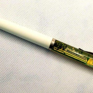 Könnte beinhalten: Ein weißer Stift mit einem durchsichtigen, grünlichen Schaft, der ein Landschaftsbild zeigt. Der Stift hat eine weiße Kappe und eine silberne Klammer.