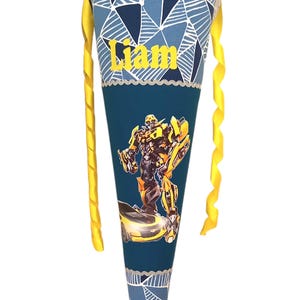 Puede incluir: Un cono escolar azul y amarillo con un personaje de Bumblebee Transformer y el nombre "Liam" en él.