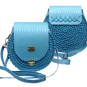 Könnte beinhalten: Zwei hellblaue runde Umhängetaschen mit einem gehäkelten Design. Eine Tasche hat eine Klappe mit Schlangenhautmuster und einem Metallverschluss. Die andere Tasche hat eine Klappe mit einem gestickten Design.