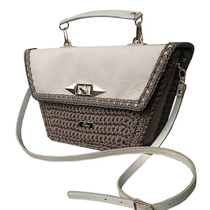 Könnte beinhalten: Eine weiße und braune gehäkelte Handtasche mit einer Lederklappe und einem goldenen Verschluss. Die Tasche hat einen weißen Ledertragegurt.