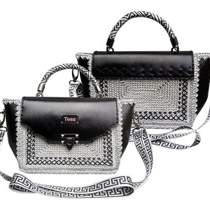 Könnte beinhalten: Zwei schwarze Ledertaschen mit silbernem und schwarzem Häkelbesatz und einem schwarz-weißen Musterband. Die kleinere Tasche trägt den Namen "Tess" auf der Vorderseite.