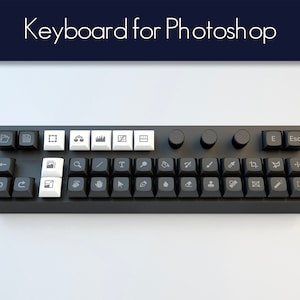 Könnte beinhalten: Eine schwarze Tastatur mit weißen Tasten und grauen Symbolen für Photoshop. Die Tastatur hat zwei Knöpfe oben rechts.