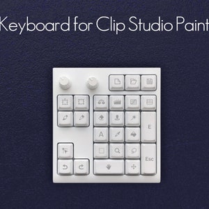 May include: White keyboard with a variety of keys and icons for use with Clip Studio Paint software. The keys include icons for tools such as a pen, brush, eraser, and selection tools. The keyboard also has a few function keys, such as "Esc" and "E".
