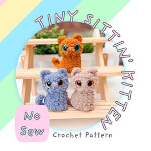 Op de afbeelding: Drie kleine gehaakte kittens van oranje, grijs en beige garen met grote plastic ogen. De tekst TINY SITTIN' KITTEN en No Sew Crochet Pattern is zichtbaar. De kittens staan op een lichte houten standaard met groen blad in de achtergrond.