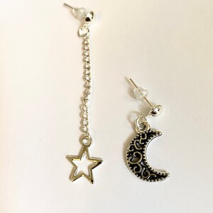 May include: A pair of silver earrings with a dangling star charm and a crescent moon charm. The earrings are made of metal and have a silver finish.