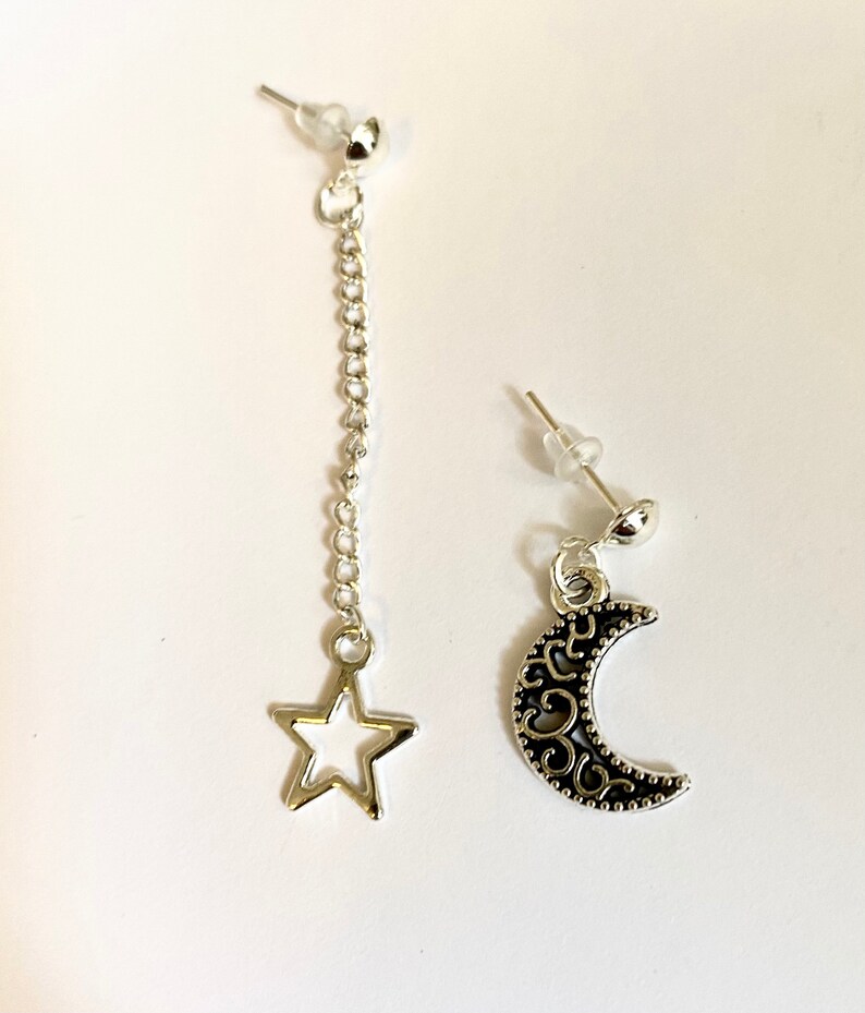 May include: A pair of silver earrings with a dangling star charm and a crescent moon charm. The earrings are made of metal and have a silver finish.
