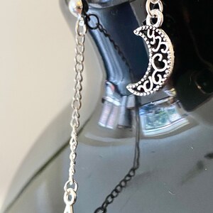 May include: A pair of silver earrings with a crescent moon charm and a star charm dangling from a chain.