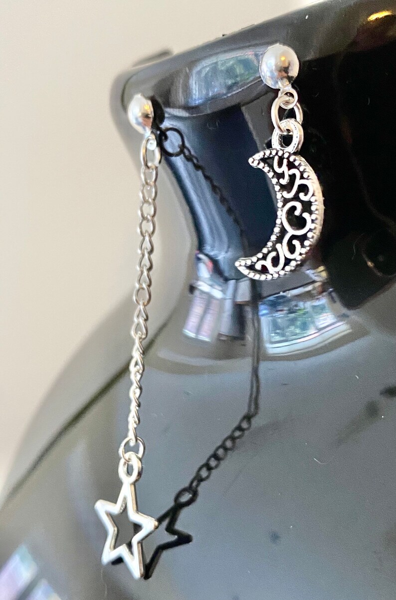May include: A pair of silver earrings with a crescent moon charm and a star charm dangling from a chain.