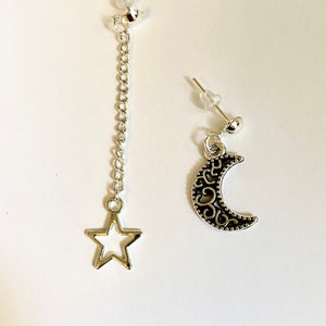 May include: A pair of silver earrings with a dangling star and crescent moon charm. The earrings are on a white background.