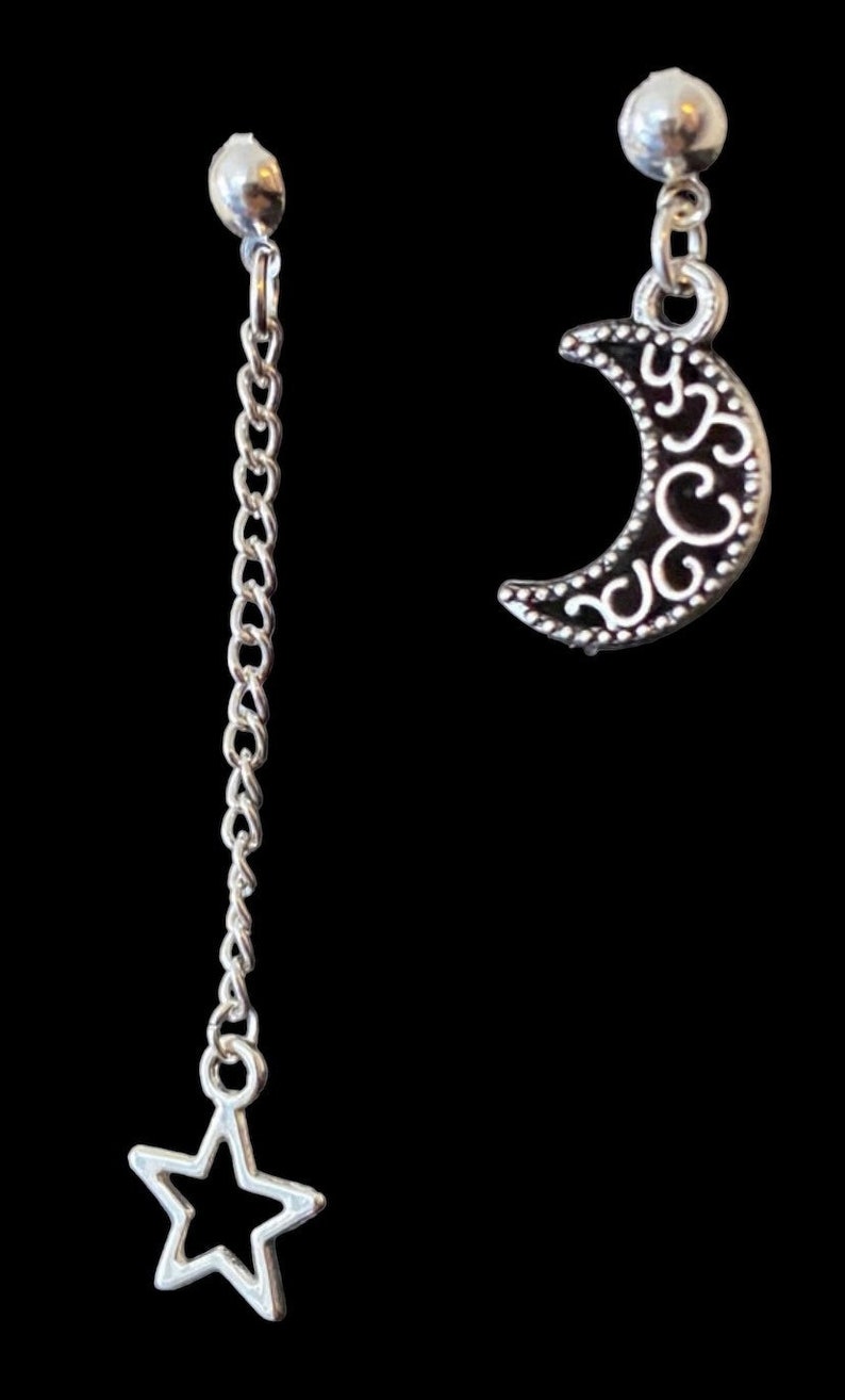 May include: A pair of silver earrings, one with a crescent moon charm and the other with a star charm hanging from a chain.