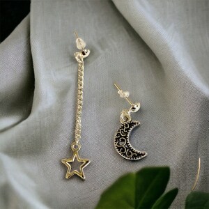 May include: A pair of silver earrings with a star and crescent moon design. The star earring has a long chain attached to it.