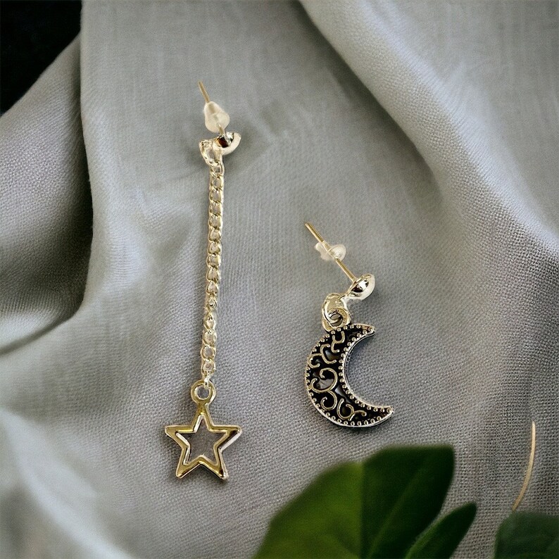 May include: A pair of silver earrings with a star and crescent moon design. The star earring has a long chain attached to it.