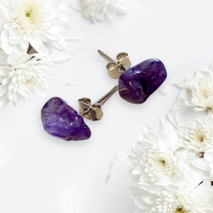 May include: A pair of amethyst gemstone earrings with silver posts. The amethyst stones are a deep purple color and have a natural, irregular shape.