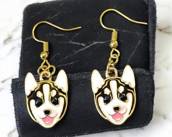 May include: A pair of gold-tone earrings featuring a black and white husky dog face charm. The earrings have a hook closure.