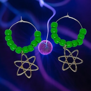 May include: A pair of green beaded hoop earrings with a gold atom charm hanging from each hoop.