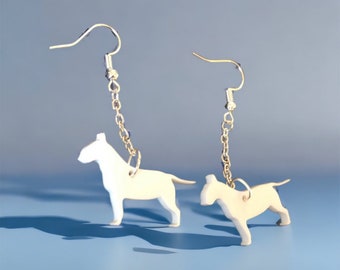 May include: A pair of silver dangle earrings featuring white bull terrier silhouettes. The earrings have a silver chain and a hook closure.