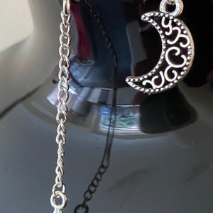 May include: A pair of silver earrings, one with a crescent moon charm and the other with a star charm hanging from a silver chain.