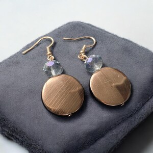 以下が含まれることがあります： 丸い磨かれたゴールドのディスクとクリアなクリスタルビーズがついたゴールドのイヤリングのペア