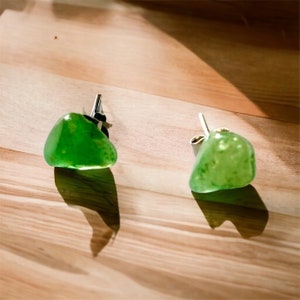 May include: A pair of green gemstone earrings with silver posts. The gemstones are irregularly shaped and have a translucent, slightly cloudy appearance.