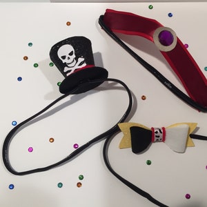 May include: Three black headbands with different decorations. One headband has a black felt pirate hat with a white skull and crossbones. Another headband has a black and white bow with a red and white polka dot accent. The third headband has a red satin crown with a purple jewel.