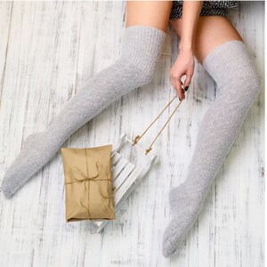 K&ouml;nnte beinhalten: Ein Paar graue Oberschenkelsocken mit einem wei&szlig;en Holzschlitten und einer braunen Geschenkbox.
