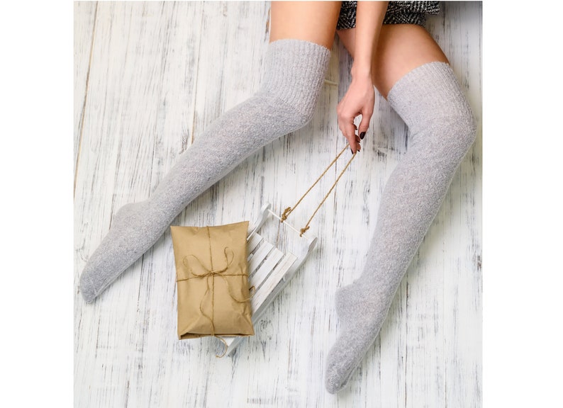 K&ouml;nnte beinhalten: Ein Paar graue Oberschenkelsocken mit einem wei&szlig;en Holzschlitten und einer braunen Geschenkbox.