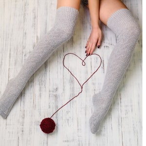 May include: A person wearing gray thigh-high socks draws a heart shape on a white wooden floor with a red ball of yarn.