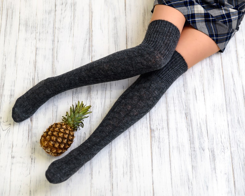 K&ouml;nnte beinhalten: Ein Paar graue Oberschenkelsocken mit einer Ananas auf einem wei&szlig;en Holzboden.