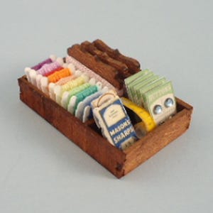 May include: A miniature wooden sewing box filled with spools of colorful thread, a small measuring tape, and packets labeled "Buttons" and "Masons Sharps". The box is made of dark wood and contains various sewing supplies.