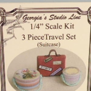 Peut inclure: Un ensemble de voyage miniature de 3 pièces, comprenant une valise rouge avec des autocollants de voyage, un récipient rond avec un motif floral et un petit récipient. Le texte indique "Georgia's Studio Line 1/4" Scale Kit 3 Piece Travel Set (Suitcase)".