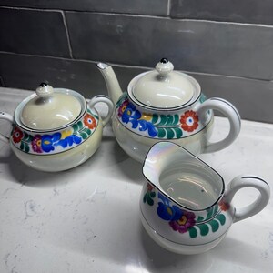 May include: A vintage tea set with a white base and colorful floral designs. The set includes a teapot, creamer, and sugar bowl.