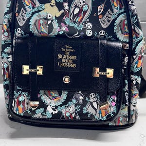May include: Black backpack featuring a repeating pattern of characters from "The Nightmare Before Christmas." The front flap has a black buckle closure and the text "Tim Burton's The Nightmare Before Christmas."