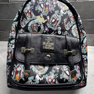 May include: Black backpack featuring characters from "The Nightmare Before Christmas." The bag has a flap closure with silver-tone hardware and adjustable straps. The design includes Jack Skellington, Sally, and other characters.