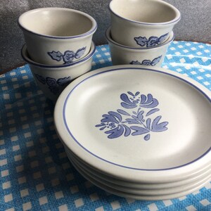 Pode incluir: Um conjunto de quatro xícaras de cerâmica branca com desenhos florais azuis, empilhadas umas sobre as outras. As xícaras estão sobre uma toalha de mesa quadriculada azul e branca. Há também quatro pratos de cerâmica branca com desenhos florais azuis empilhados uns sobre os outros.