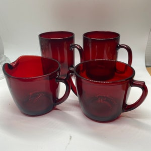 Peut inclure: Ensemble de quatre tasses en verre rouge avec des poignées et un pichet en verre rouge assorti. Les tasses et le pichet ont une forme légèrement arrondie.